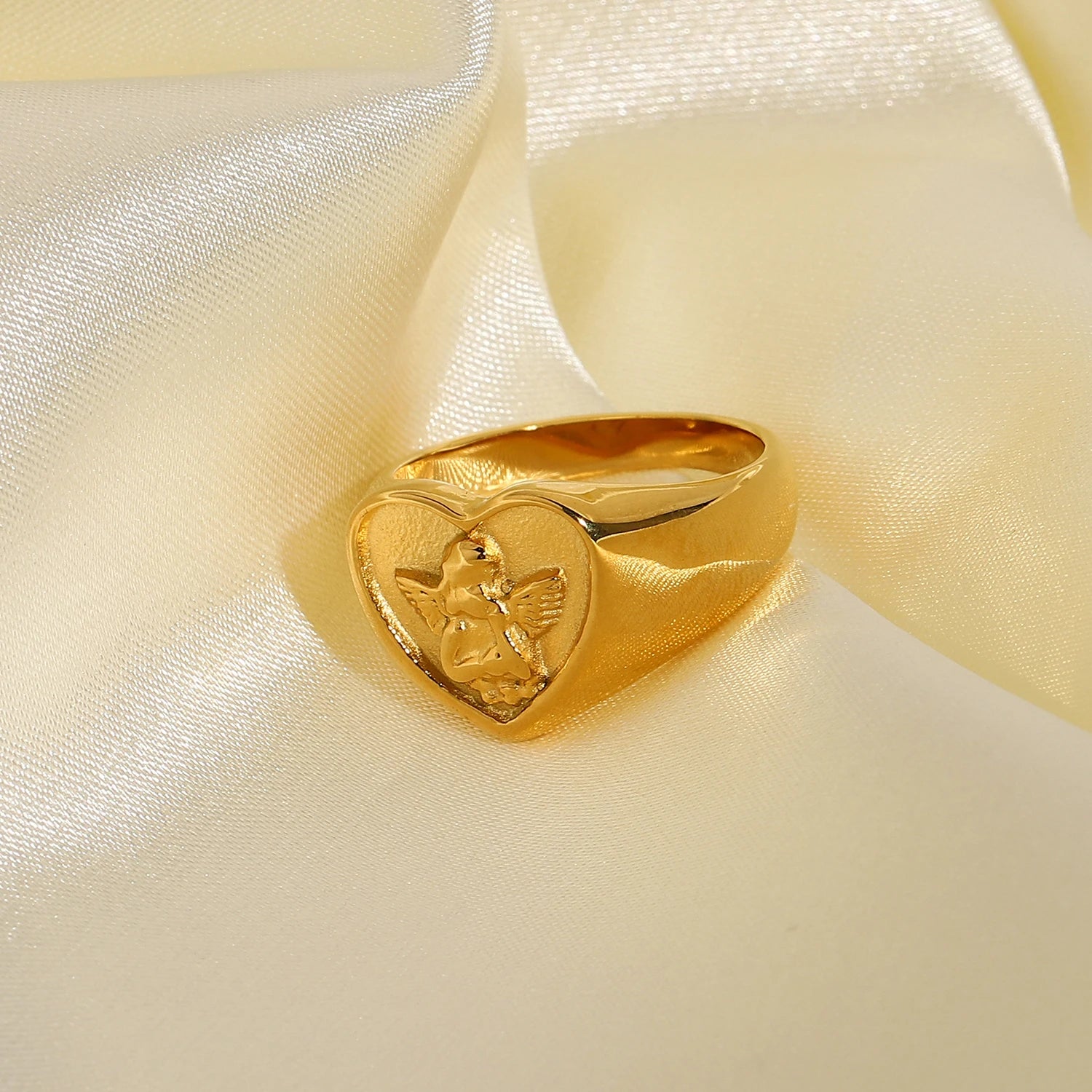 A chunky 18ct gold plated medical steel heart signet ring featuring a detailed embossed cherub (angel) on a textured gold background.