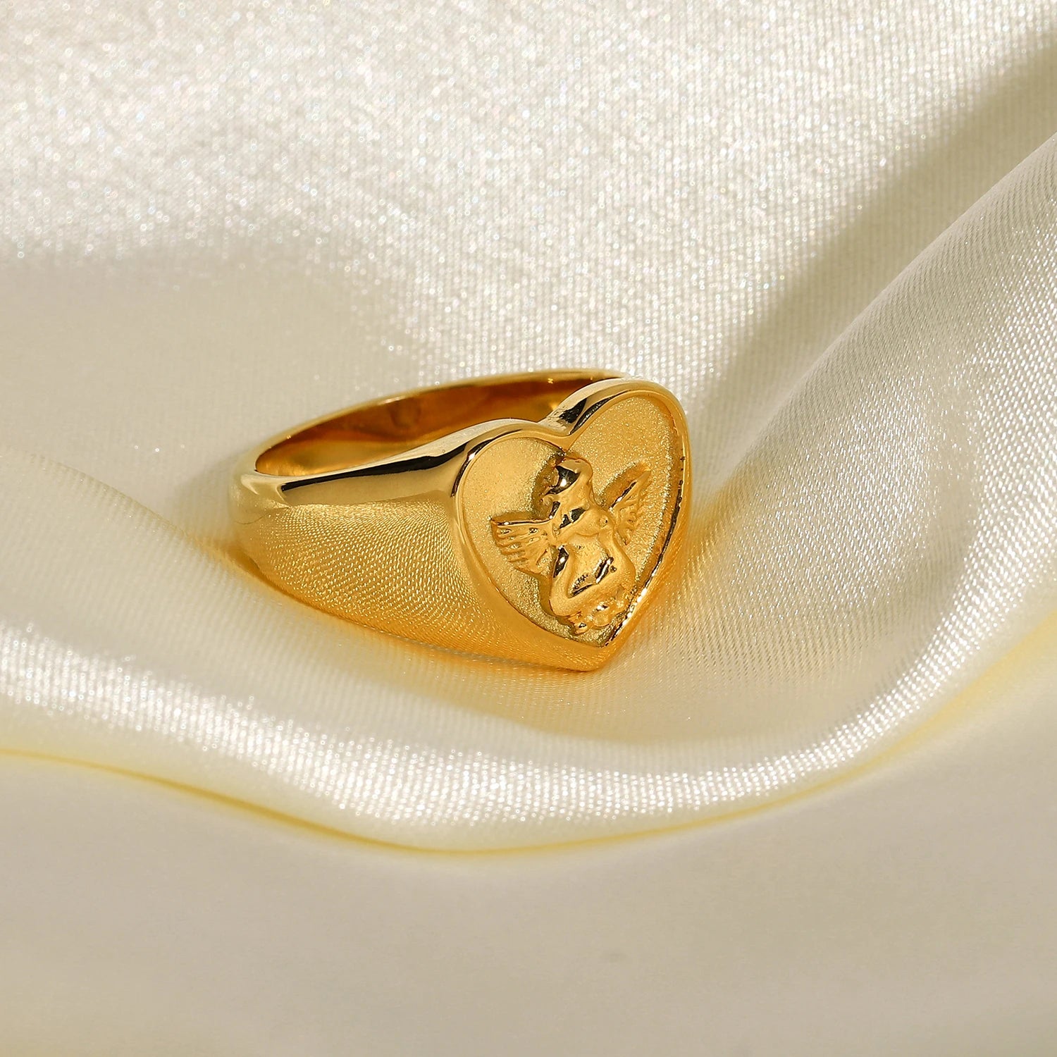 A chunky 18ct gold plated medical steel heart signet ring featuring a detailed embossed cherub (angel) on a textured gold background.