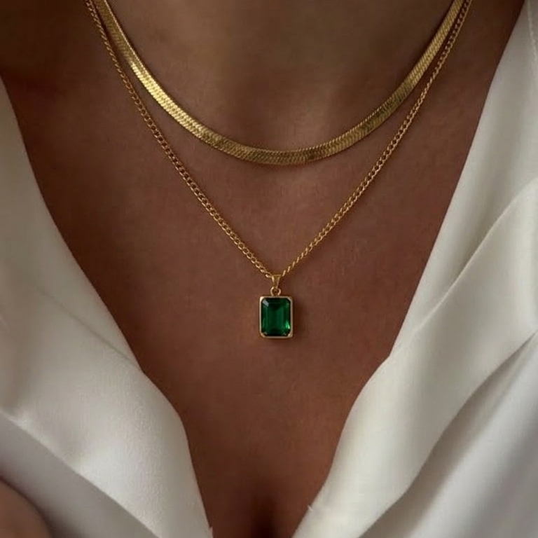 Gold necklace with a green gemstone pendant on a person wearing a white blouse.