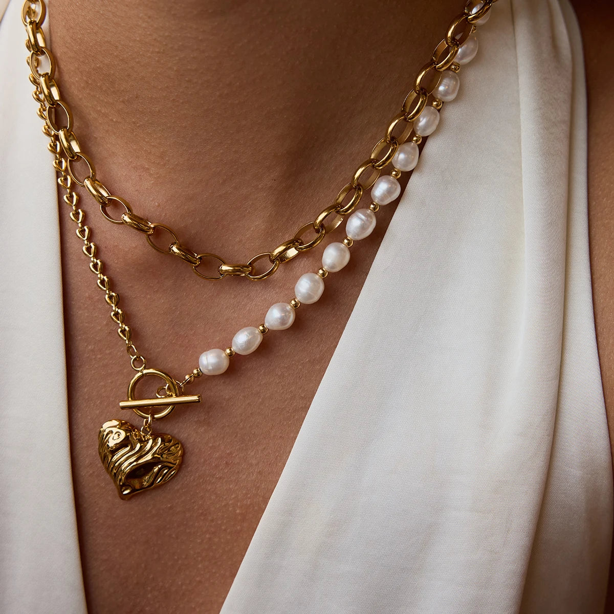 Gold chain necklace with a heart-shaped pendant worn by a person against a white background