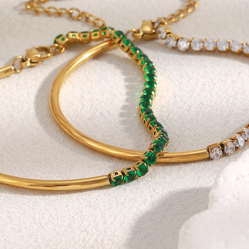 Gold bangles with green gemstones and white stones on a light background