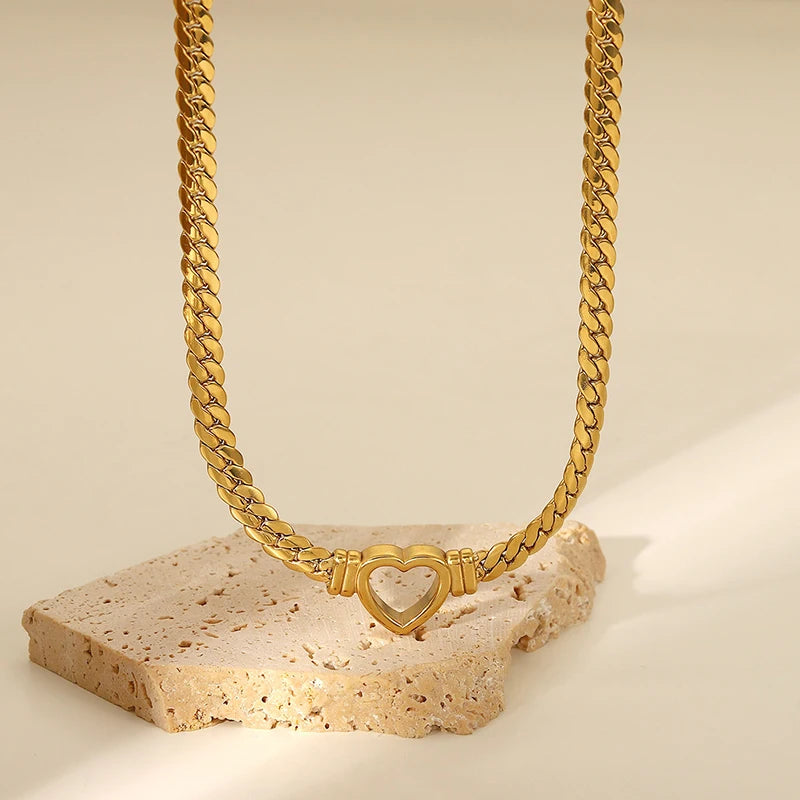 Gold chain necklace with a heart-shaped clasp on a beige stone surface