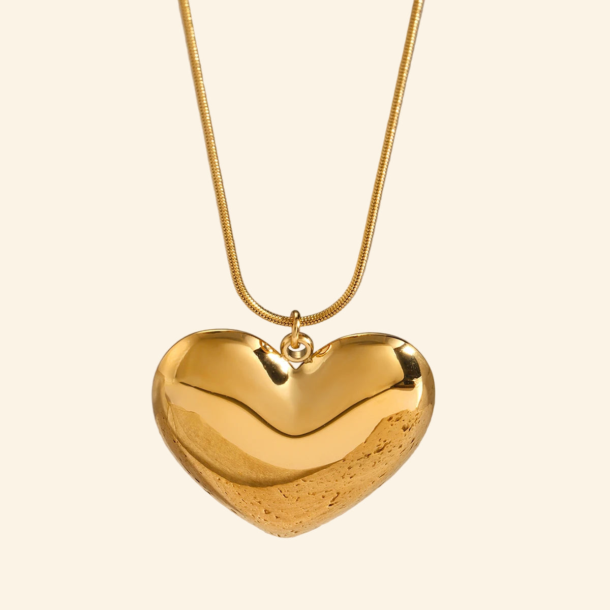 Gold heart-shaped pendant on a beige stone surface with a neutral background