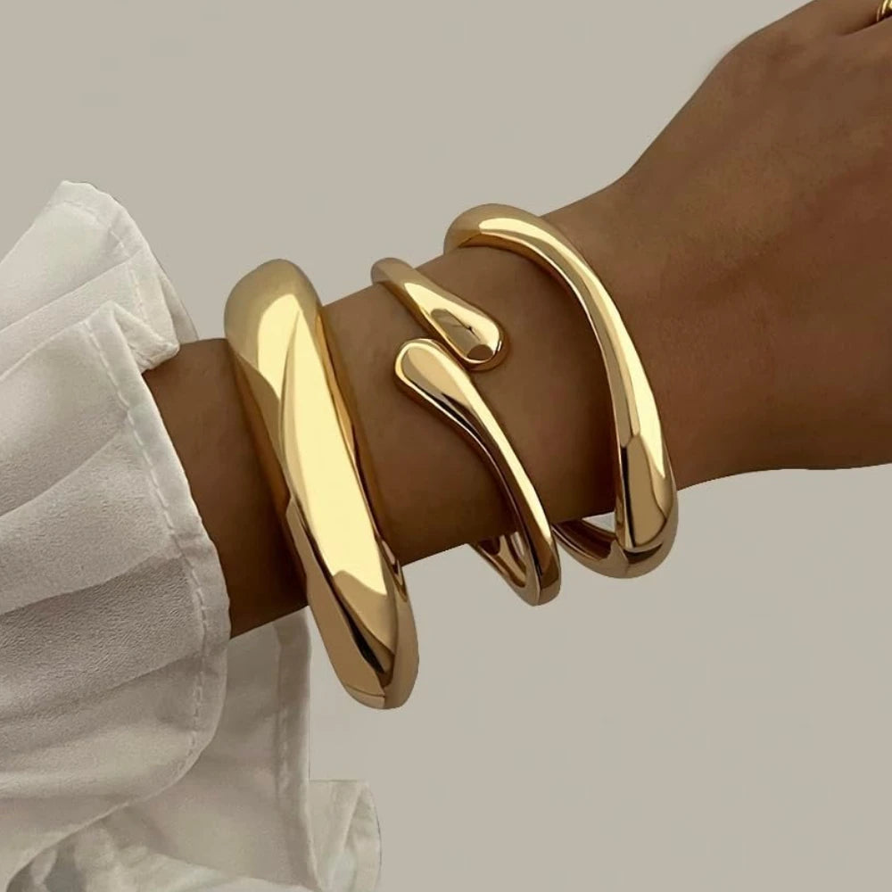 A trio of polished gold-tone bangles in varying thicknesses, featuring a sculptural organic shape and hinged closures for a stacked jewellery look.