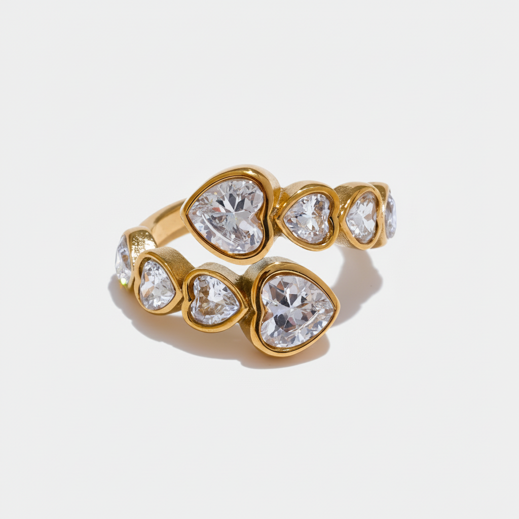 Adjustable bypass ring crafted from 18k gold plated stainless steel, featuring sparkling clear heart-shaped diamantes in a textured gold setting.