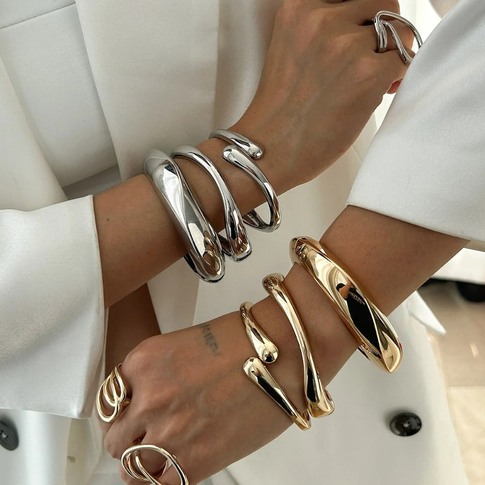 Three chunky gold-finish stackable bangles with a smooth, high-shine surface and unique curved design, displayed against a white background.