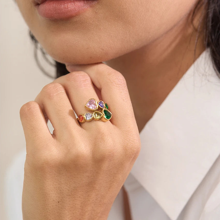 A gold-tone wrap ring featuring a bypass design set with multi-coloured heart-shaped crystals, including pink, purple, emerald green, and amber tones.