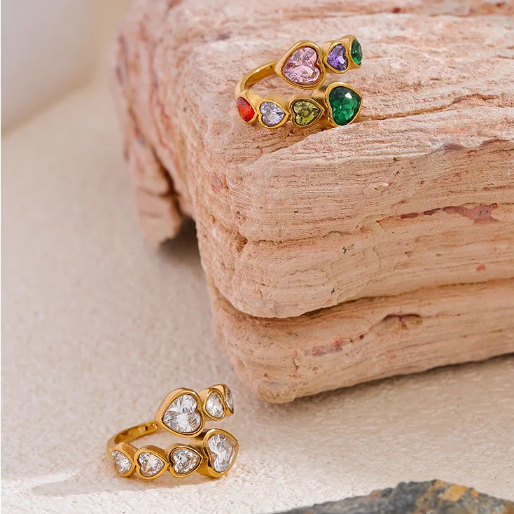 A gold-tone wrap ring featuring a bypass design set with multi-coloured heart-shaped crystals, including pink, purple, emerald green, and amber tones.