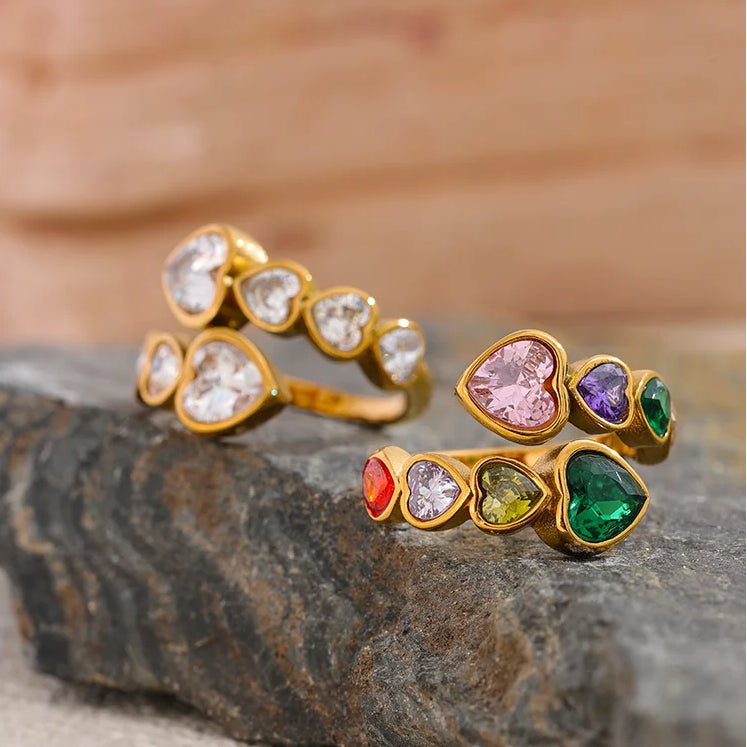 A gold-tone wrap ring featuring a bypass design set with multi-coloured heart-shaped crystals, including pink, purple, emerald green, and amber tones.