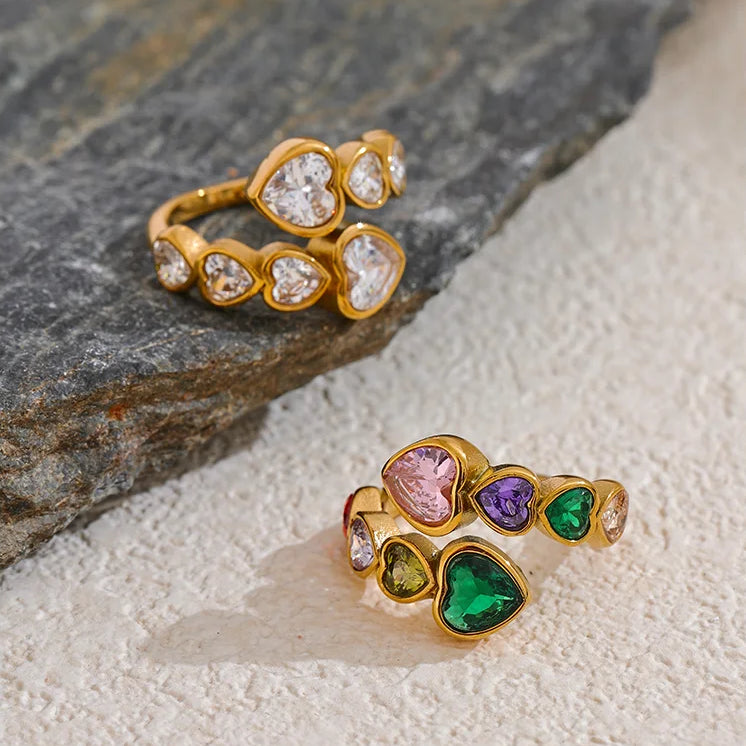A gold-tone wrap ring featuring a bypass design set with multi-coloured heart-shaped crystals, including pink, purple, emerald green, and amber tones.