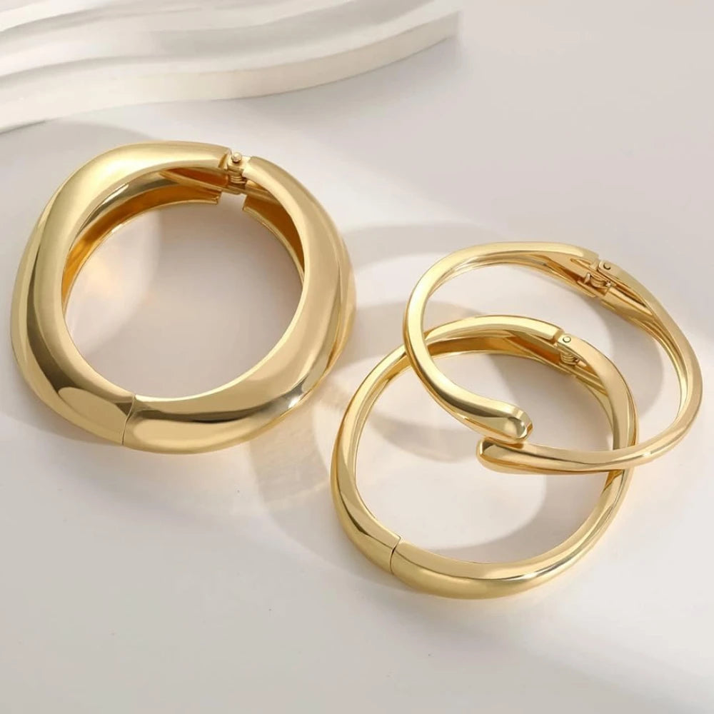 Three chunky gold-finish stackable bangles with a smooth, high-shine surface and unique curved design, displayed against a white background.