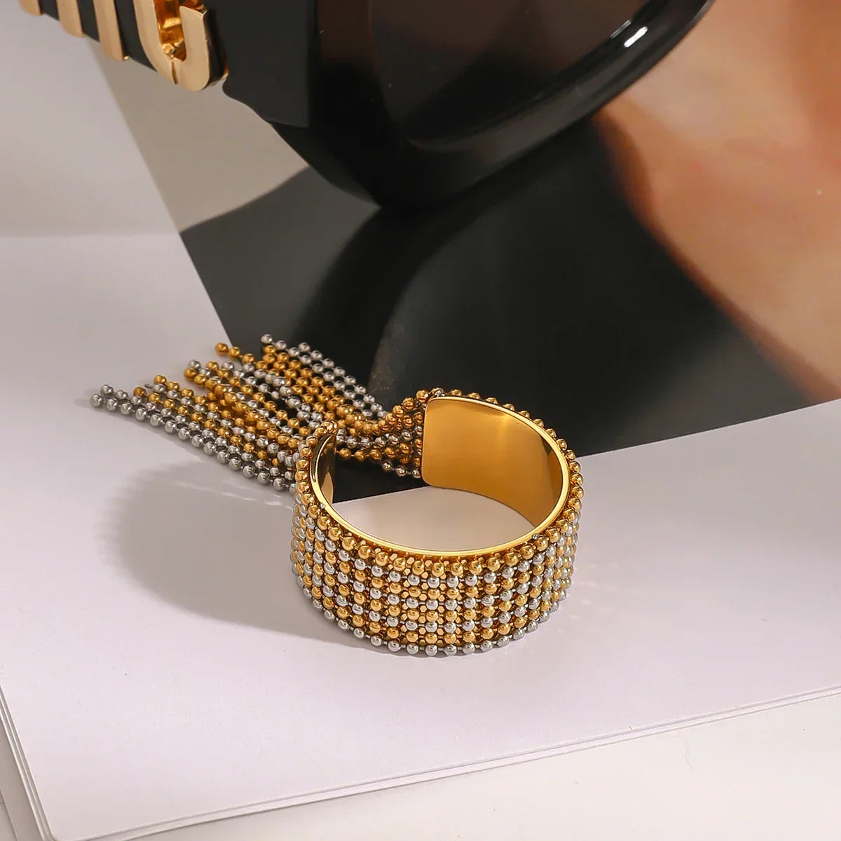 Architectural mixed-metal ring in 18k gold and silver tones, featuring a bicolour cascading ball-chain tassel for a liquid-like effect.