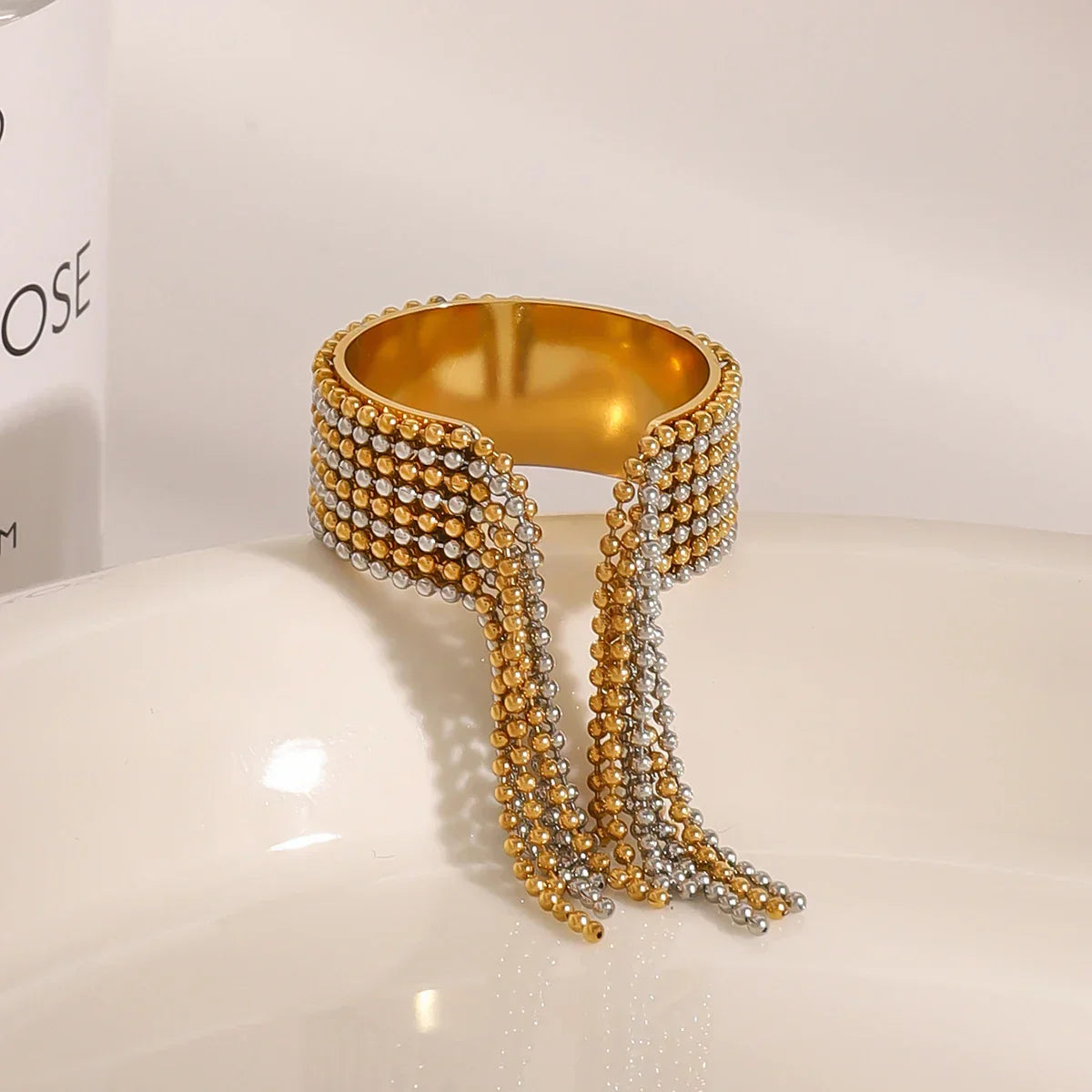 Architectural mixed-metal ring in 18k gold and silver tones, featuring a bicolour cascading ball-chain tassel for a liquid-like effect.
