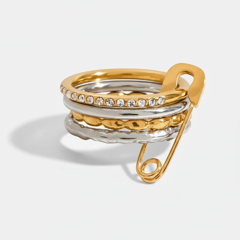 Multi-layered mixed metal stacking ring featuring alternating gold and silver-tone bands, set with clear crystals, and finished with a decorative gold safety pin. 
