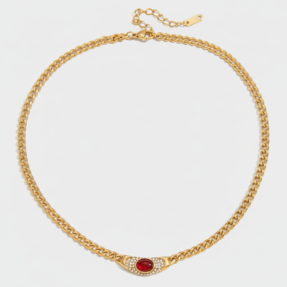 A vintage-inspired curb chain necklace in 18ct gold plated medical steel, featuring a central ruby-red cabochon stone surrounded by sparkling pavé crystals..