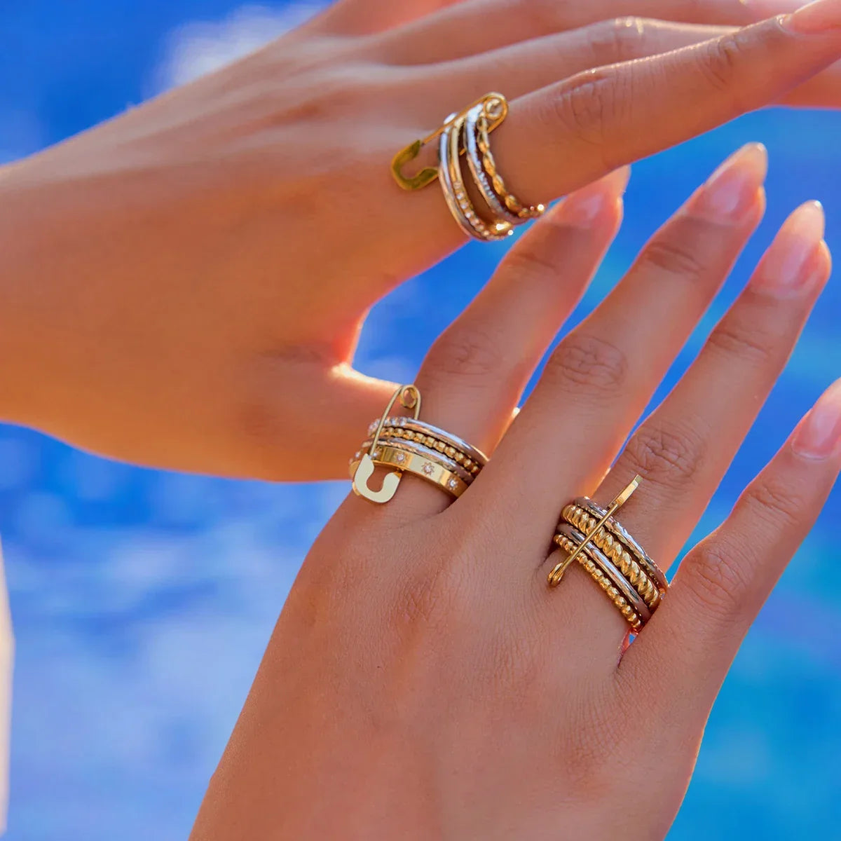 Four-band gold and silver-tone stacking ring with crystals and a safety pin detail.