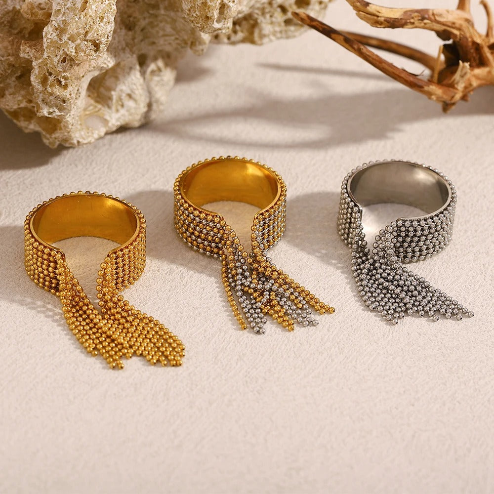 Three beaded rings in gold and silver on a textured surface with natural elements.