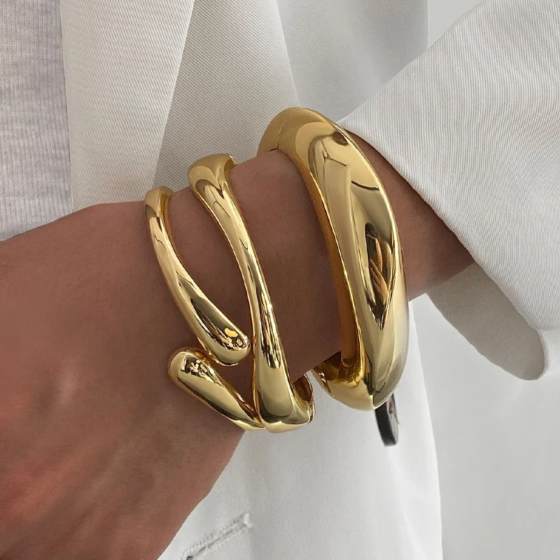 Three chunky gold-finish stackable bangles with a smooth, high-shine surface and unique curved design, displayed against a white background.