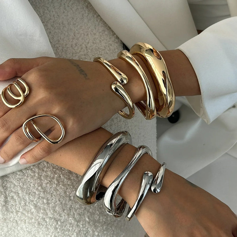 A trio of polished gold or silver-tone bangles in varying thicknesses, featuring a sculptural organic shape and hinged closures for a stacked jewellery look.