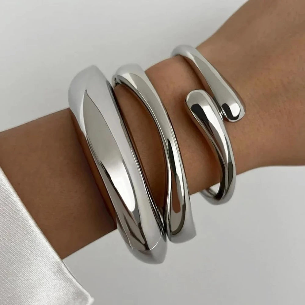 A trio of polished silver-tone bangles in varying thicknesses, featuring a sculptural organic shape and hinged closures for a stacked jewellery look.