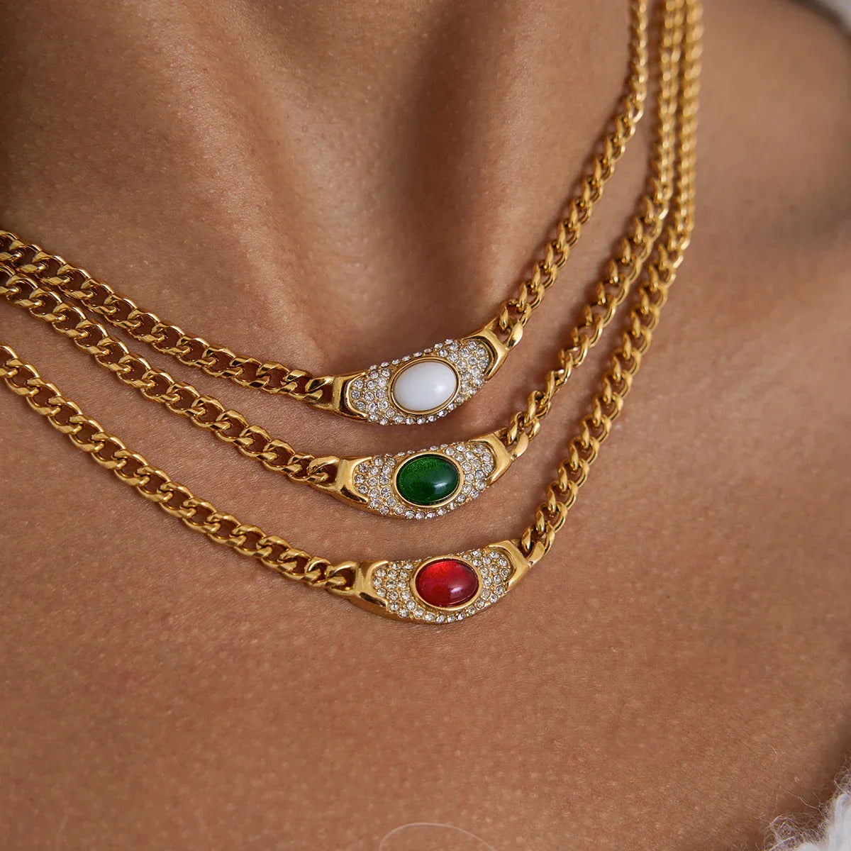 A vintage-inspired curb chain necklace in 18ct gold plated medical steel, featuring a central emerald-green cabochon stone surrounded by sparkling pavé crystals..