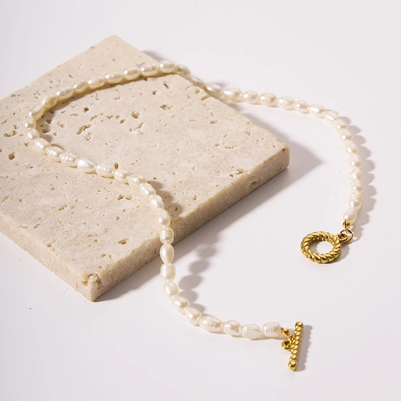 A multi-strand choker necklace featuring five rows of delicate white seed pearls and a central 18ct gold plated medical steel floral motif with an iridescent stone centre.